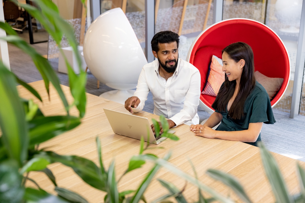Two workers chat at a laptop
